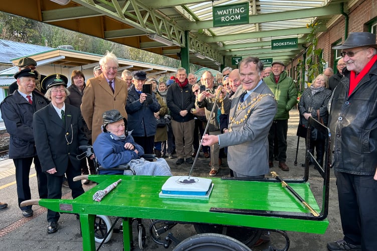 Okehampton mayor Allenton Fisher cuts the Dartmoor Line 3rd birthday cake with his ceremonial navy sword, watched by all those who helped the railway return to the town