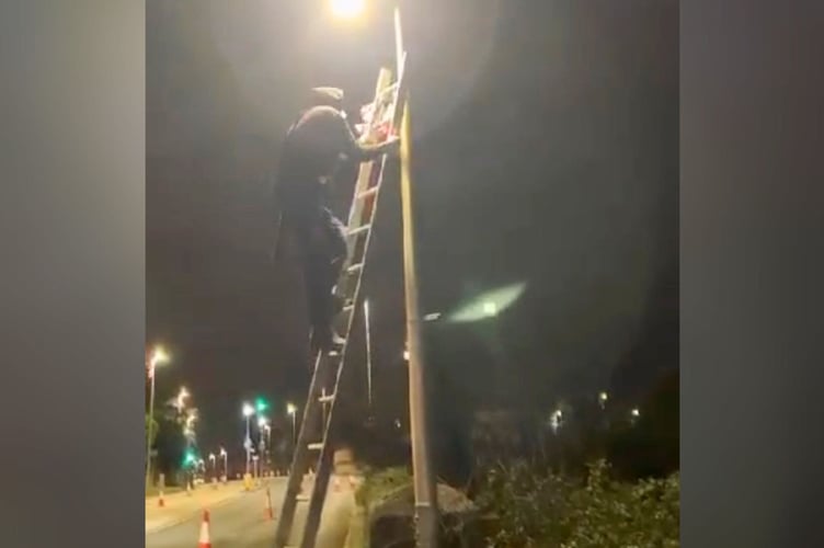 A still image from footage of a man reattaching flags to lampposts in Exeter moments after they had been removed