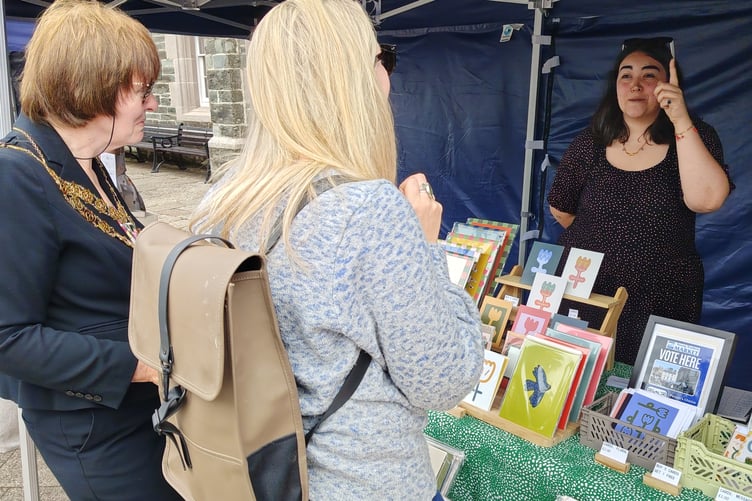 Tavistock Mayor Cllr Anne Johnson and another judge awarding points to an artist selling her creations at the SW finals of the young market traders competition in the town.