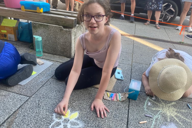 Young artists decorating Tavistock high street for the Lions Carnival Week pavement art competition. A girl chalks some golden flowers for the theme 'golden moments'.